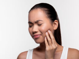 Mulher com dor facial, segurando a bochecha.