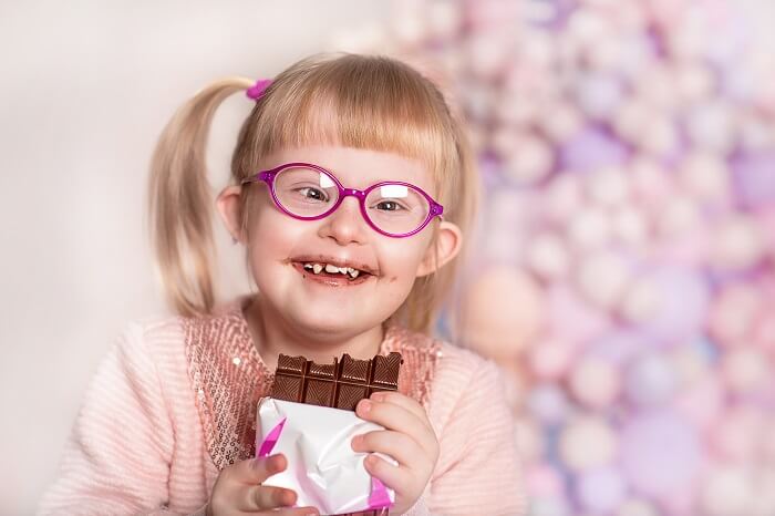 Criança com síndrome de Down sorrindo, com barra de chocolate na mão.