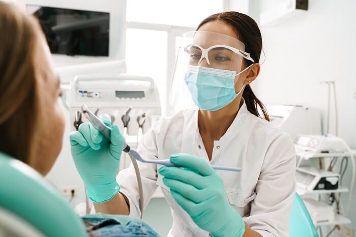 Dentista com equipamentos de proteção atendendo paciente no consultório odontológico.