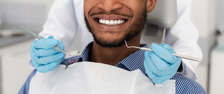 Homem negro sorrindo enquanto recebe tratamento odontológico