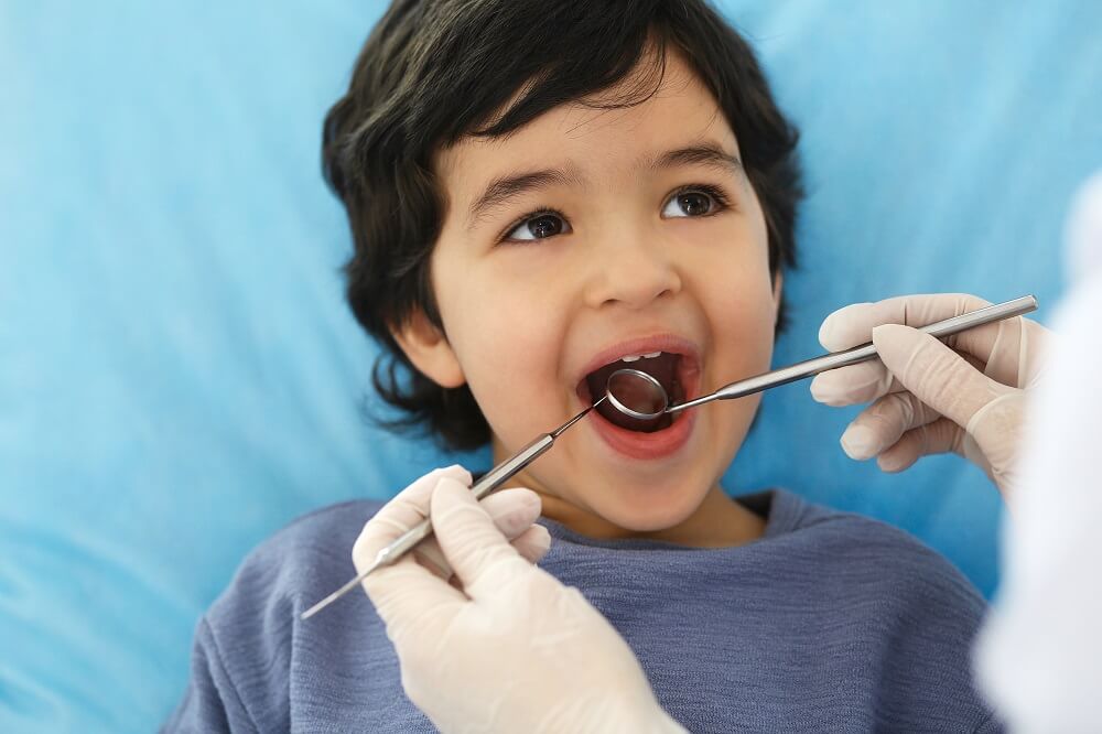 Menino com a boca aberta enquanto é examinado por dentista