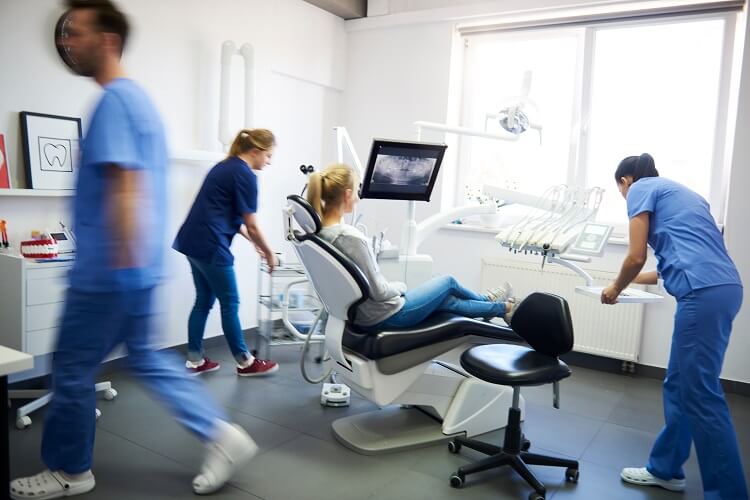 Mulher sentada em cadeira odontológica com equipe de dentistas ao redor