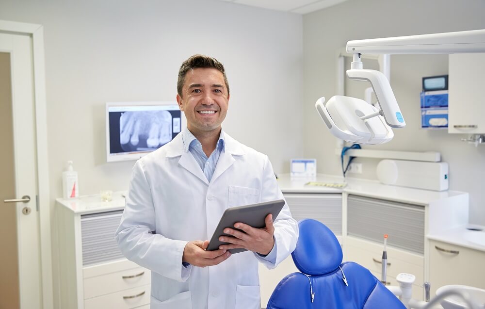 Dentista sorrindo em pé dentro de consultório
