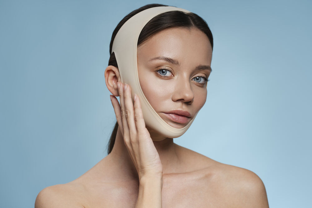 Mulher com faixa de compressão facial após cirurgia estética no rosto.