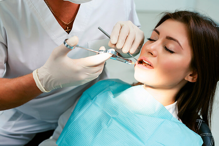 dentista aplicando tratamento com ozonioterapia na odontologia em uma paciente do gênero feminino branca com cabelos castanhos lisos.