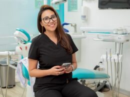 Dentista com celular na mão em consultório odontológico.