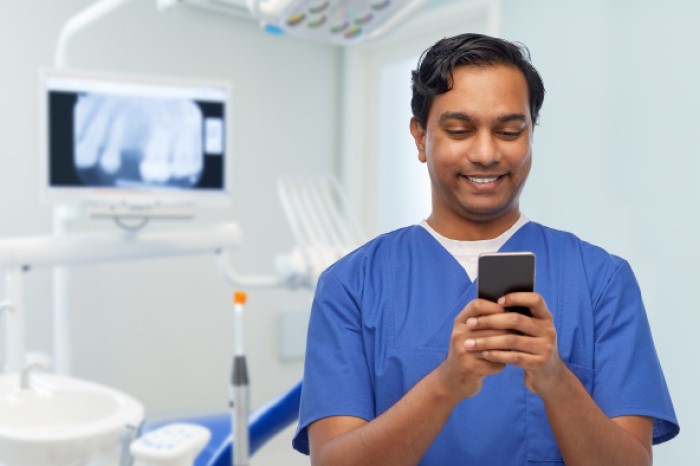 Dentista rindo com celular na mão em consultório odontológico.