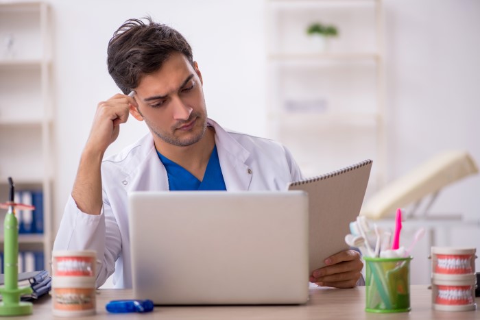 Dentista lendo no notebook e em caderno resumos de odontologia.