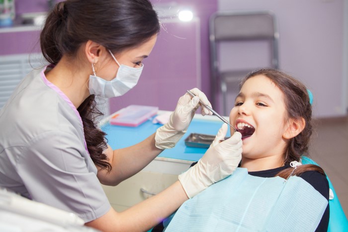 Jovem dentista realiza atendimento a criança.
