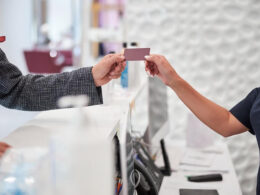 Secretária de dentista entregando cartão de visita de dentista para paciente.