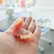 Dentista com prótese dentária na mão em consultório odontológico.
