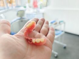 Dentista com prótese dentária na mão em consultório odontológico.