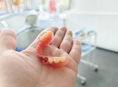 Dentista com prótese dentária na mão em consultório odontológico.