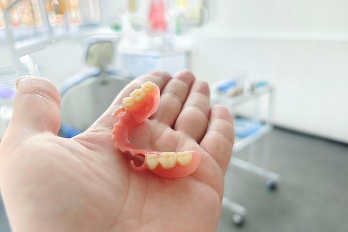Dentista com prótese dentária na mão em consultório odontológico.