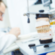 Dentista fazendo prótese com articulador odontológico à frente.