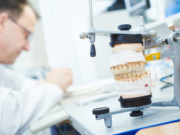 Dentista fazendo prótese com articulador odontológico à frente.