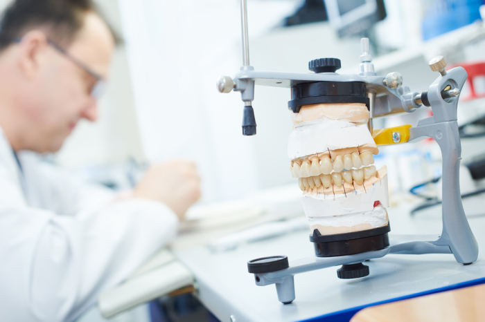 Dentista fazendo prótese com articulador odontológico à frente.