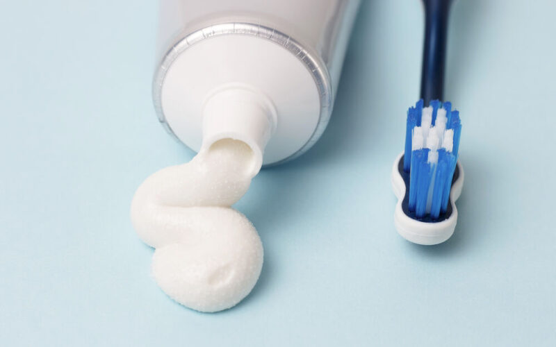 Creme dental e escova de dentes sobre fundo azul.