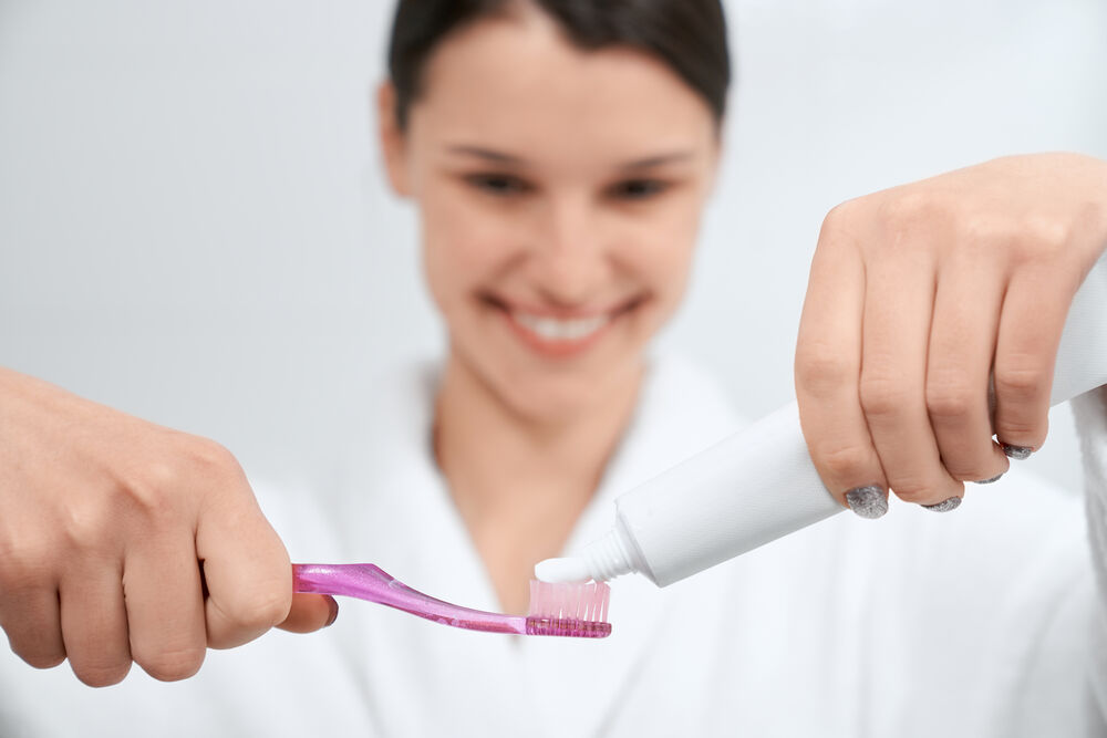 Mulher sorrindo enquanto coloca creme dental em uma escova de dentes.